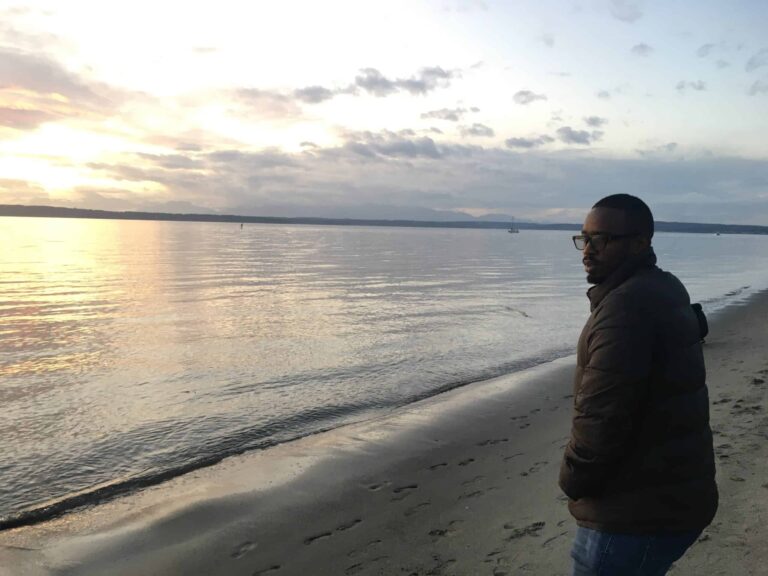 Person standing on the beach looking at the ocean during sunset